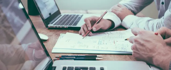 Business professionals reviewing documents and notes at a desk with laptops.