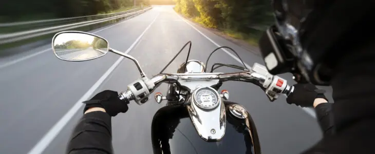 The motorcyclist is riding through the empty asphalt road in the evening